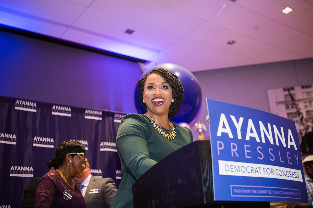 Ayanna Pressley smiles at the podium while speaking to a crowd on her victory election night party.