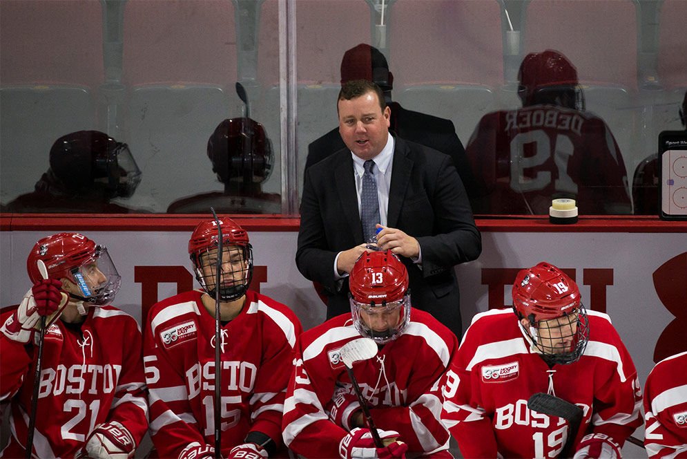 BU men's ice hockey head coach Albie O'Connell talks to a player on the bench during a game.