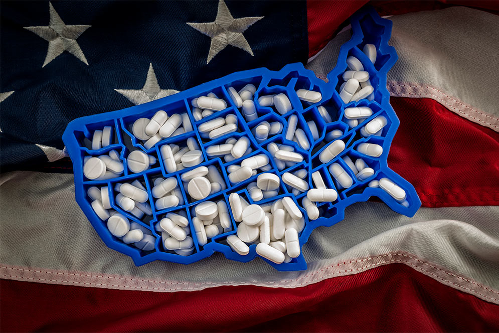 Concept photo of a United States shaped pill box holding a lot of pills resting on an American flag, symbolizing the opioid crisi in America