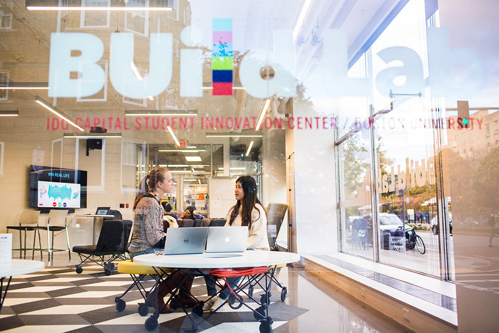 A BU student works with her Hub cocurricular supervisor, seen through the window of the BUildLab: IDG Capital Student Innovation Center at Boston University.