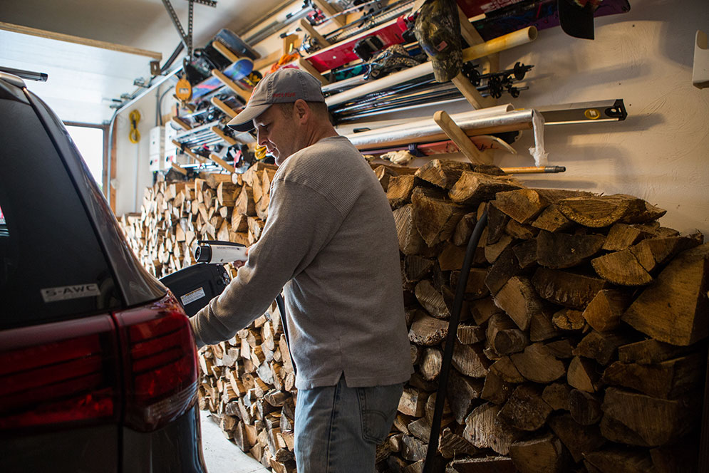 Mike Wagner inserts a charging plug into his Mitsubishi Outlander PHEV hybrid vehicle.