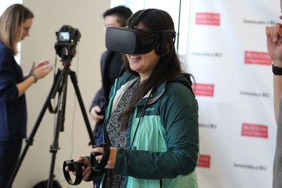 A woman smiles while using a Virtual Reality head set and hand controls at the BU ARVR Festival.