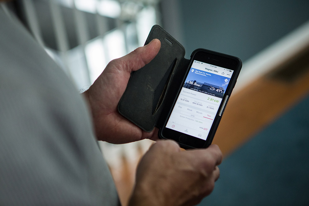 Mike Wagner holds his smartphone showing his home's solar system dashboard app.