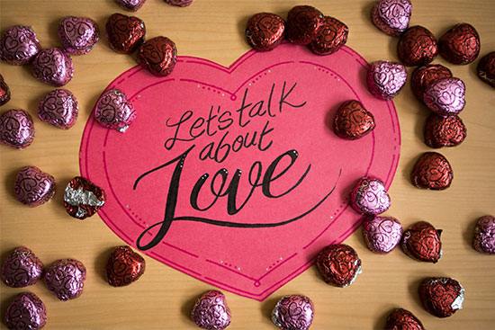 Paper valentine greeting that says "Let's Talk About Love" surrounded by chocolate hearts.