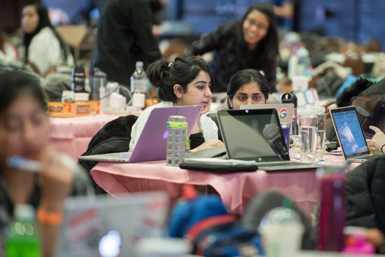 two students working at a table full of laptops