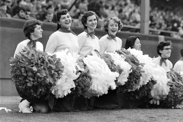 cheerleaders with pom poms kneel on the field at a football game