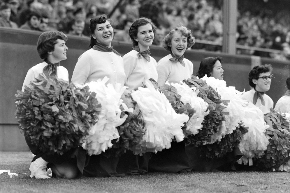 cheerleaders with pom poms kneel on the field at a football game