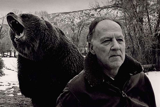 Werner Herzog with a grizzly bear roaring behind him, in grayscale