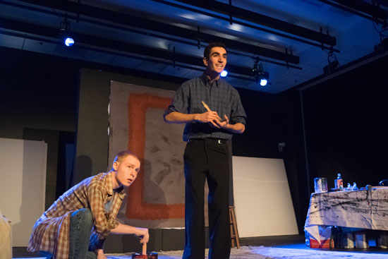 one person kneeling and another standing, both onstage and looking past the camera