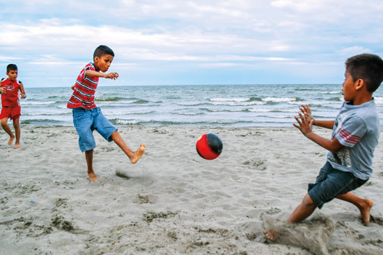 two kids playing soccer on the beach