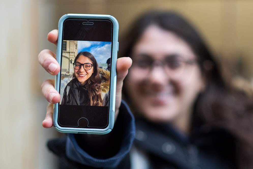Lexi Herosian holding a phone with a photo of herself on it