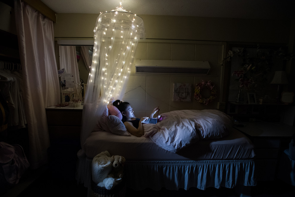 A student hangs our in her dark dorm room while watching Grey's anatomy on her phone.