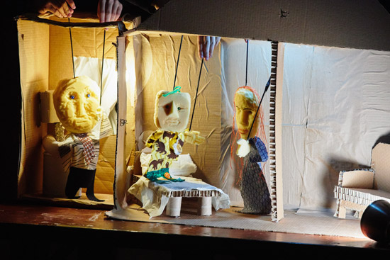 three puppets of mixed materials controlled from above in front of a cardboard set