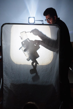 a student manipulating a scrap metal puppet behind a lit screen