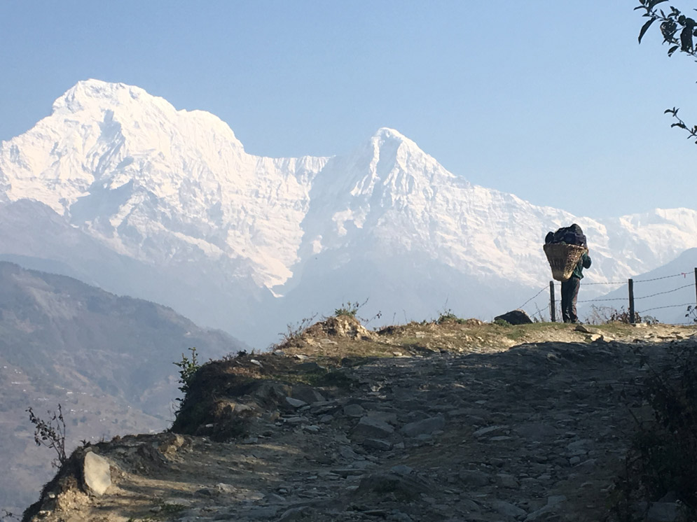 someone standing on a mountain path carrying a large pack with white mountains in the background