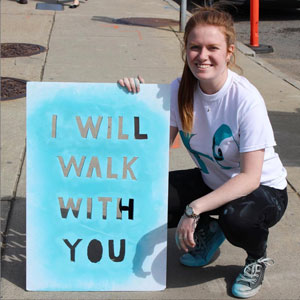 Russell holding a sidewalk stencil that says I WILL WALK WITH YOU