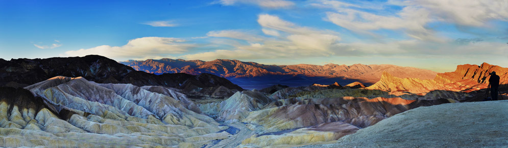 sun rays cast across a panorama of mountains; a person stands on the edge