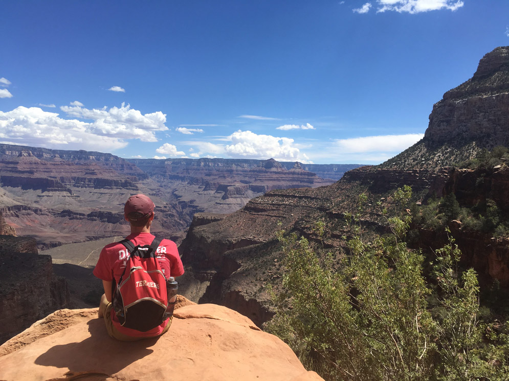 a student wearing a terrier backpack sitting on a rock looking out over canyons