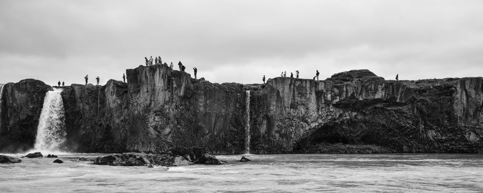 a cliff by the sea, in black and white, with people standing along the edge sightseeing