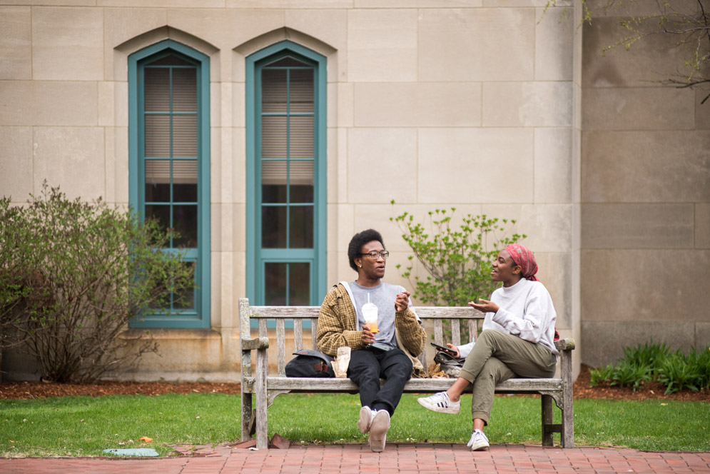 Arinze Okwuosah and Ireon Roach sitting on a bench and chatting near Marsh Chapel 
