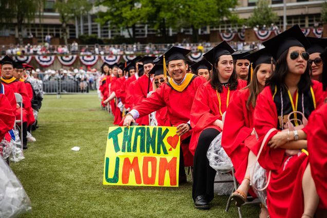 a graduate holds a sign that says THANK U MOM at commencement on Nickerson Field