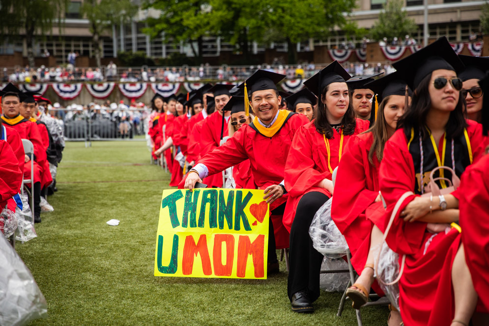a graduate holds a sign that says THANK U MOM at commencement on Nickerson Field