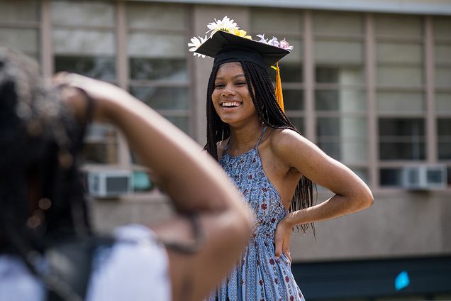 A student poses for a photo with their cap on the COM lawn