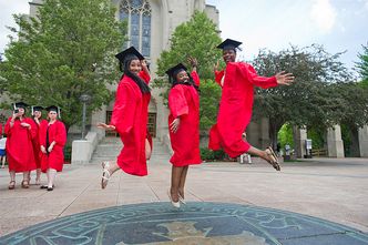 Three Boston University graduating students jump on the BU Seal symbol on Marsh Plaza on Commencement Sunday.