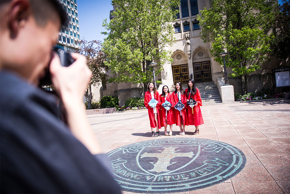 Three BU graduates pose for a photo with the BU Seal symbol, also known as the BU Crest, on Marsh Plaza, Commencement Sunday.