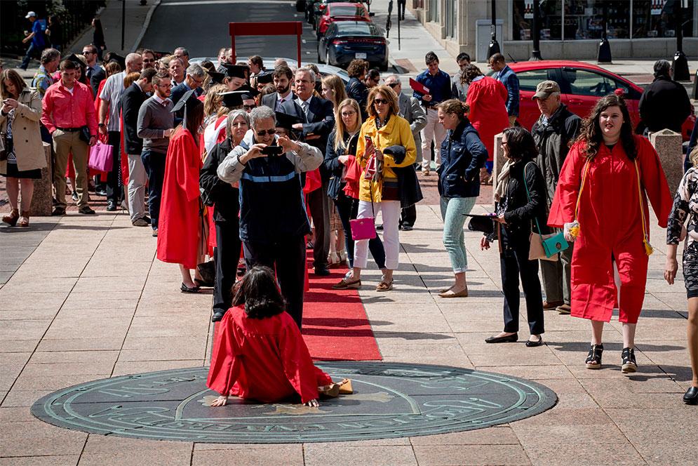 Boston University graduates and their families wait in line to take their photos stepping on the Boston University Seal symbol, also known as the Boston University Crest