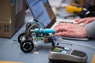 someone types code into a computer with a small robot next to them