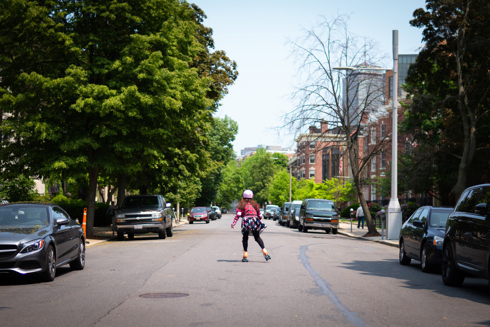 A student roller blades down a quiet street in the summertime