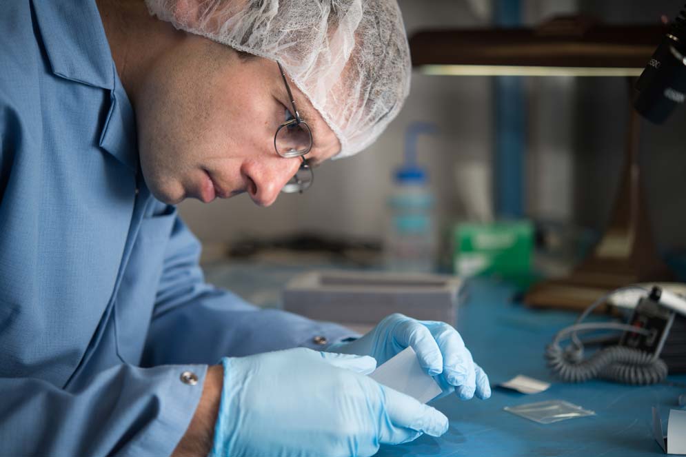 Brian Walsh of the Boston University Center for Space Physics examines a lens that will be a component of the LEXI X-ray imager.