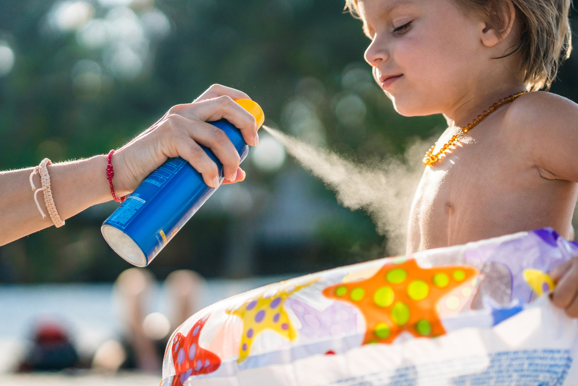 A little boy gets sprayed with sunscreen