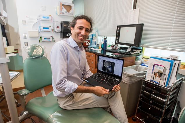 BU orthodontist Melih Motro sits on a dentist chair displaying an orthodontic x-ray on his laptop.