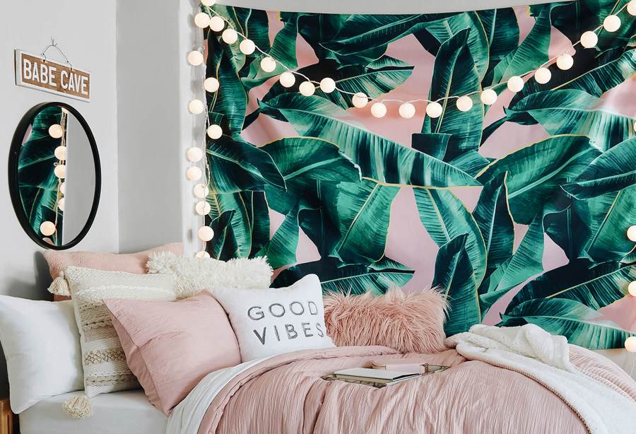 A pink and green tapestry with banana leaves hangs in a dorm room