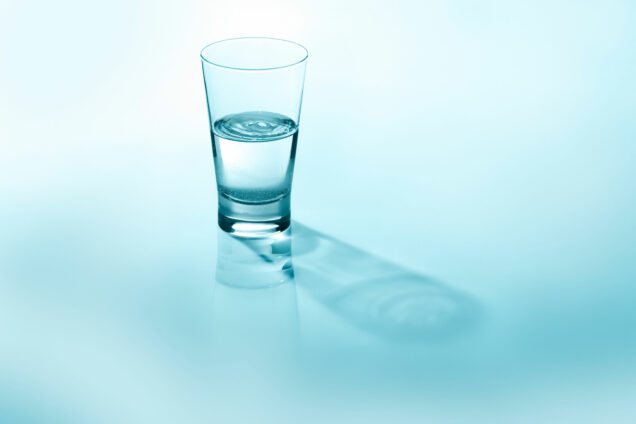 Glass of water, half full, against a light blue background.