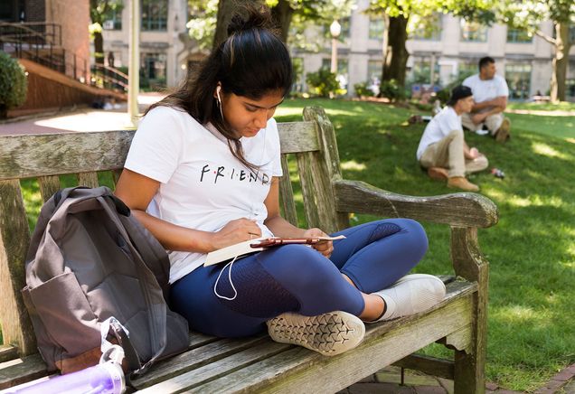 A BU student sits on a bench reading a book on the BU Beach.