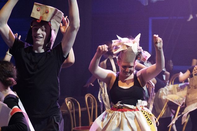 Students dance on stage wearing strange costumes made of boxes and paper