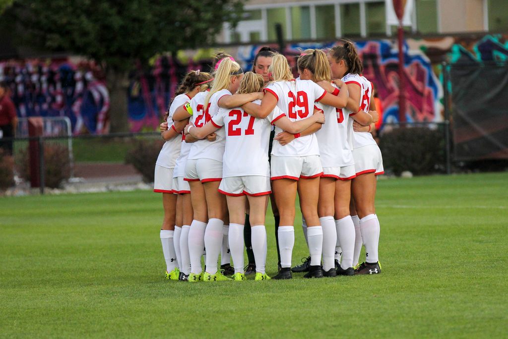 The Boston University Women's team huddles on the field during a game. 