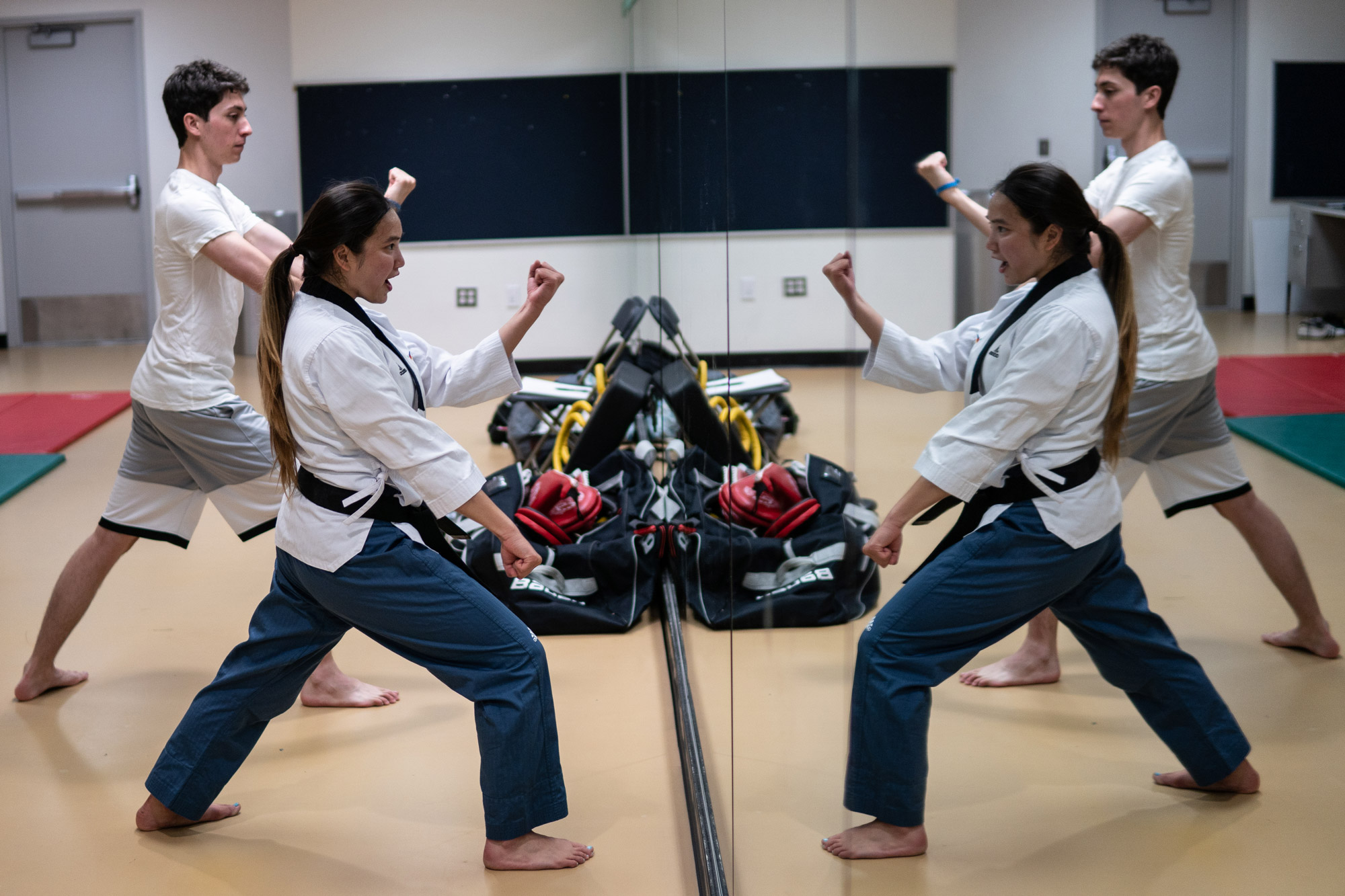 A reflection of a female and male practicing taekwondo facing a mirror