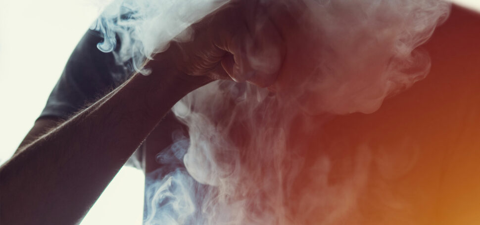 A teenager takes a hit from vaping e-cigarette blowing a cloud of vapor.