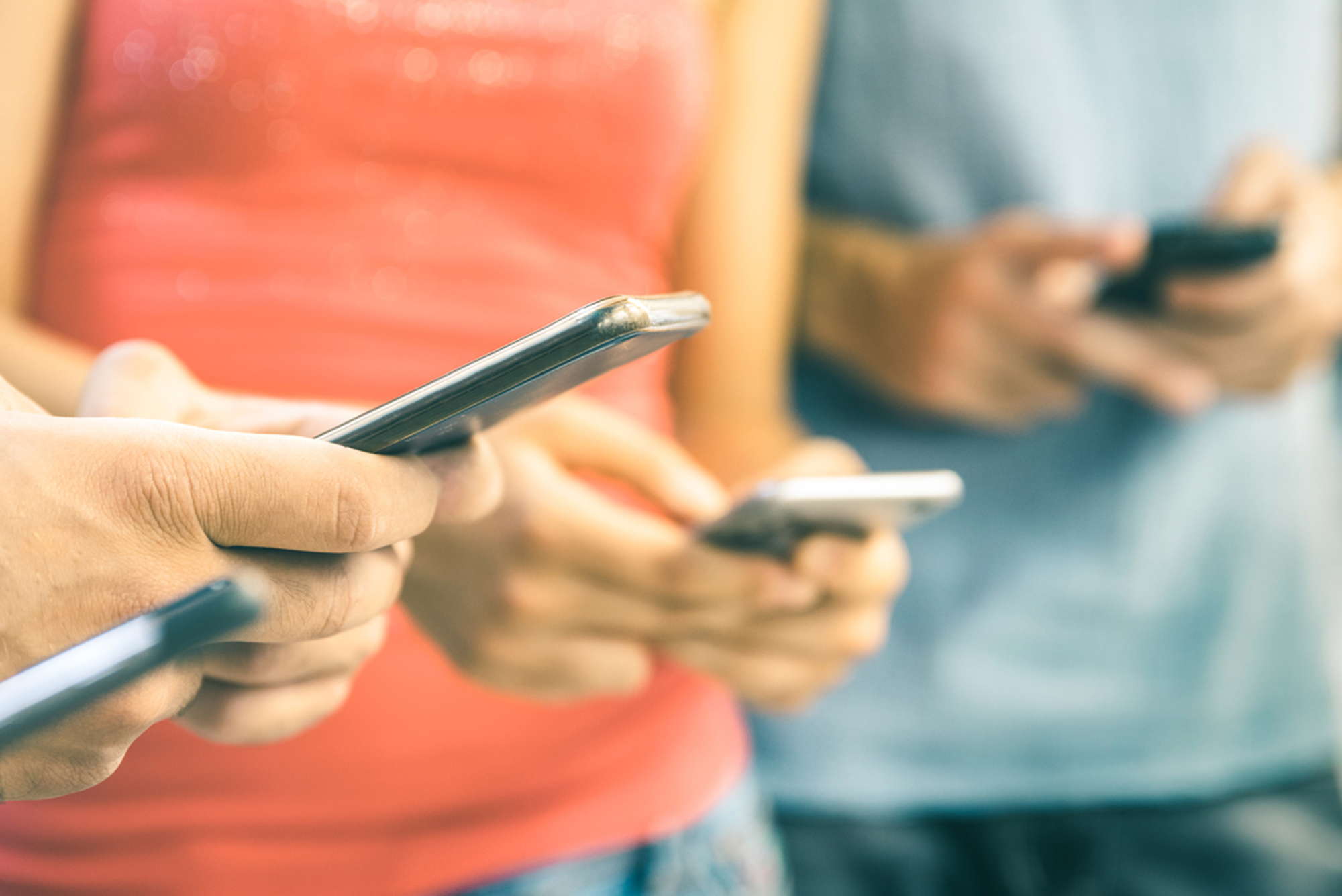 Photo: Shot of various people looking at their smartphones. Photo is zoomed in so only torsos and hands are shown.