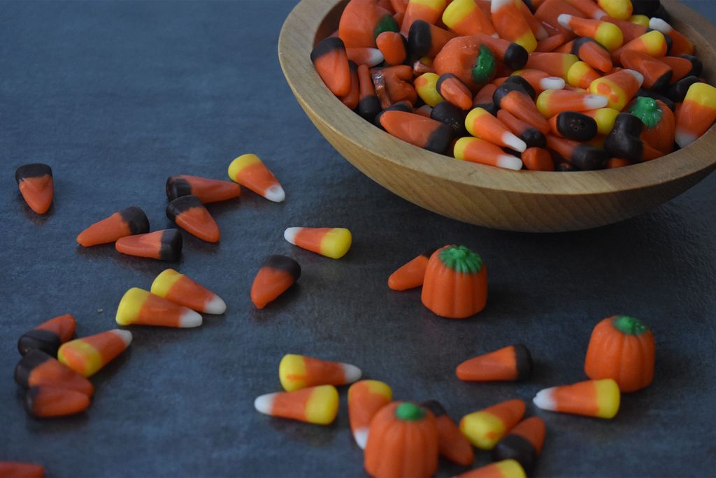 Bowl full of Halloween candy corn candies with some spilled on the table