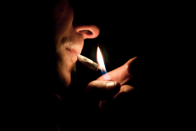 a man lights a joint with a lighter in the dark.