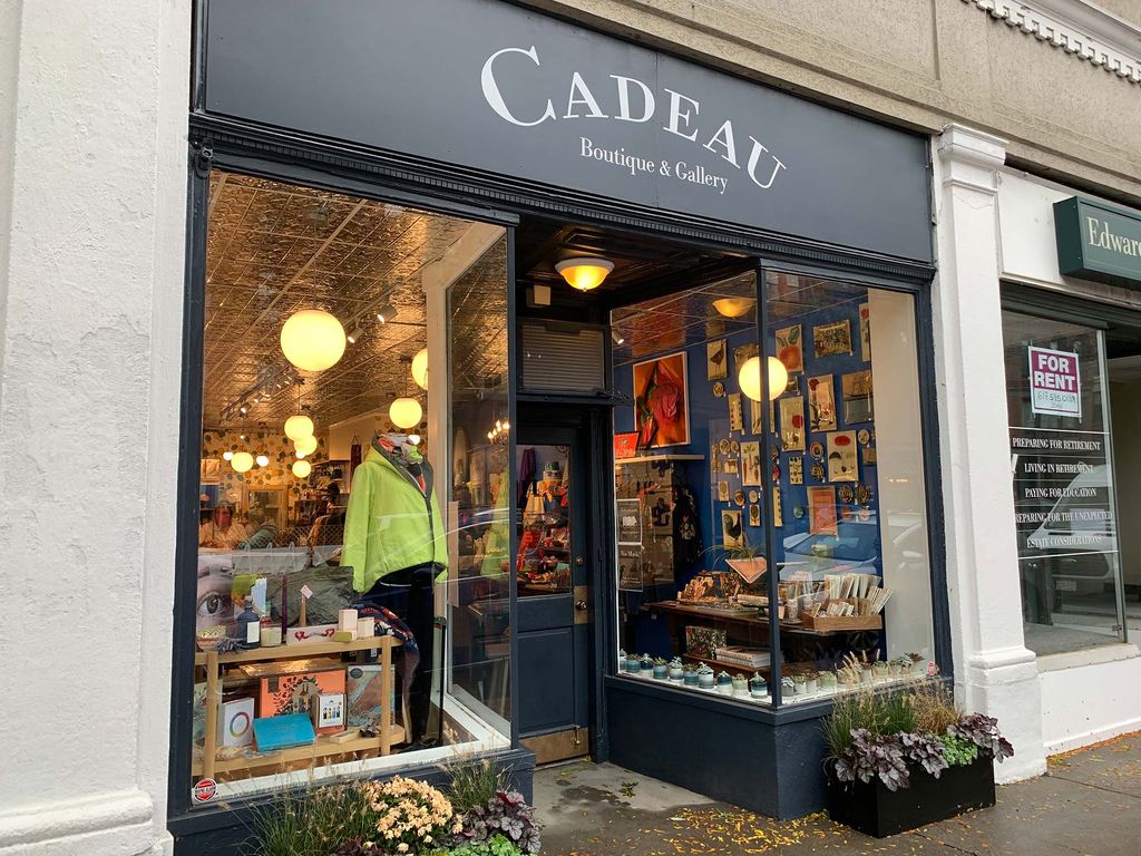 Photo of the exterior of Cadeau. A mannequin is seen and posters hang on the wall seen through the other window.