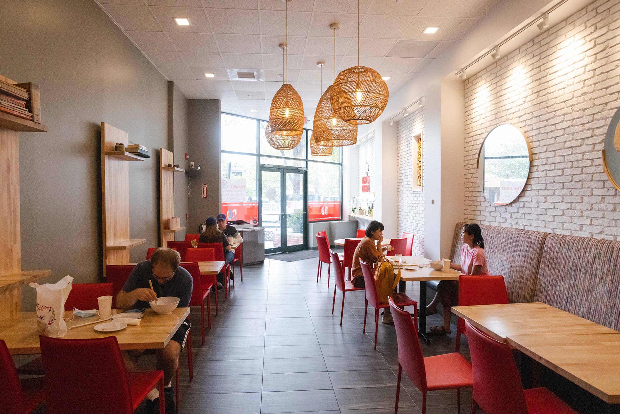 Photo from inside Dumpling Daughter (1309 Beacon St.). The chairs a red, the tables are wooden, and yellow, wicker light fixtures hang from the ceiling. A few folks eat at the tables.