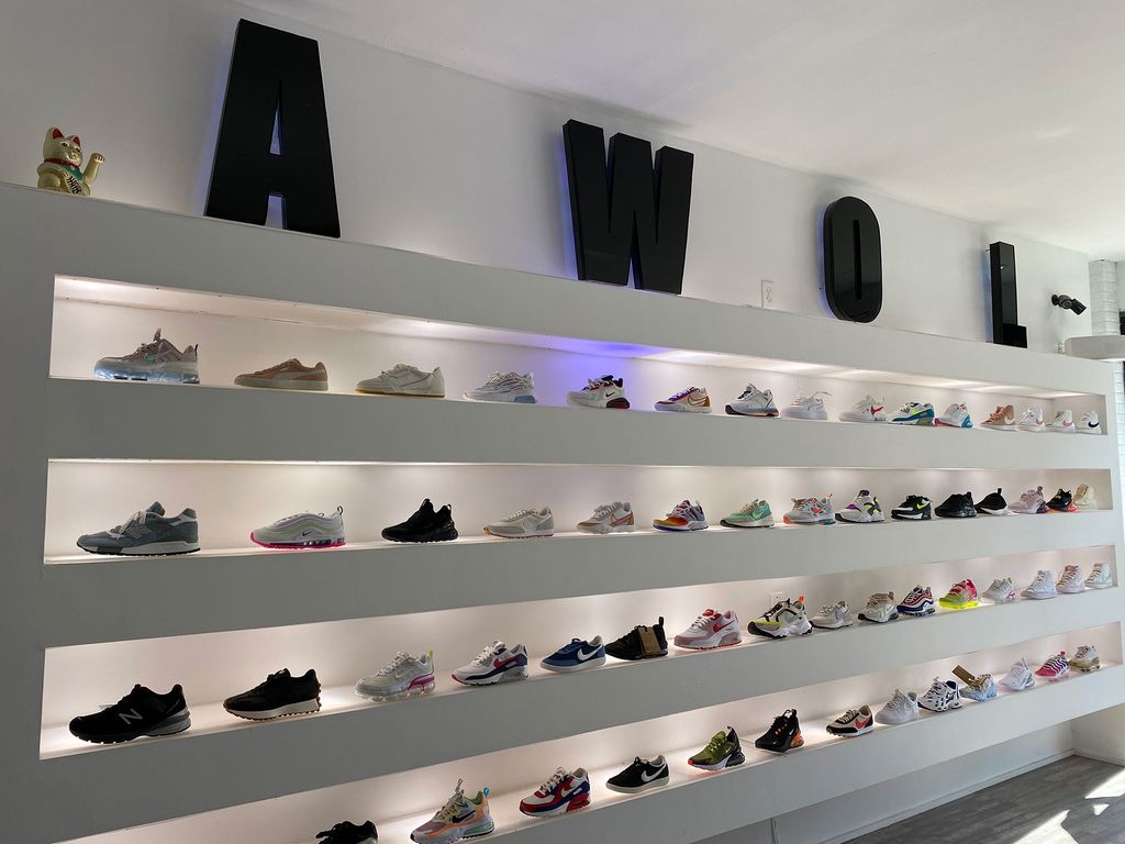 photo of a white wall with white shelves lined with different kind of sneakers. on the top shelf, large block letters in black spell out ‘AWOL.’