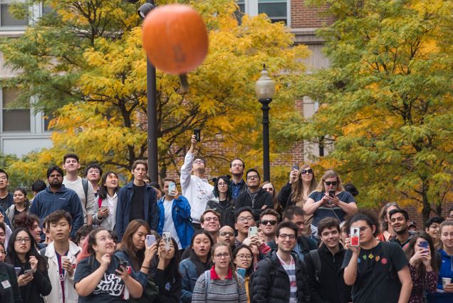 People gather and watch a pumpkin plummeting to the ground