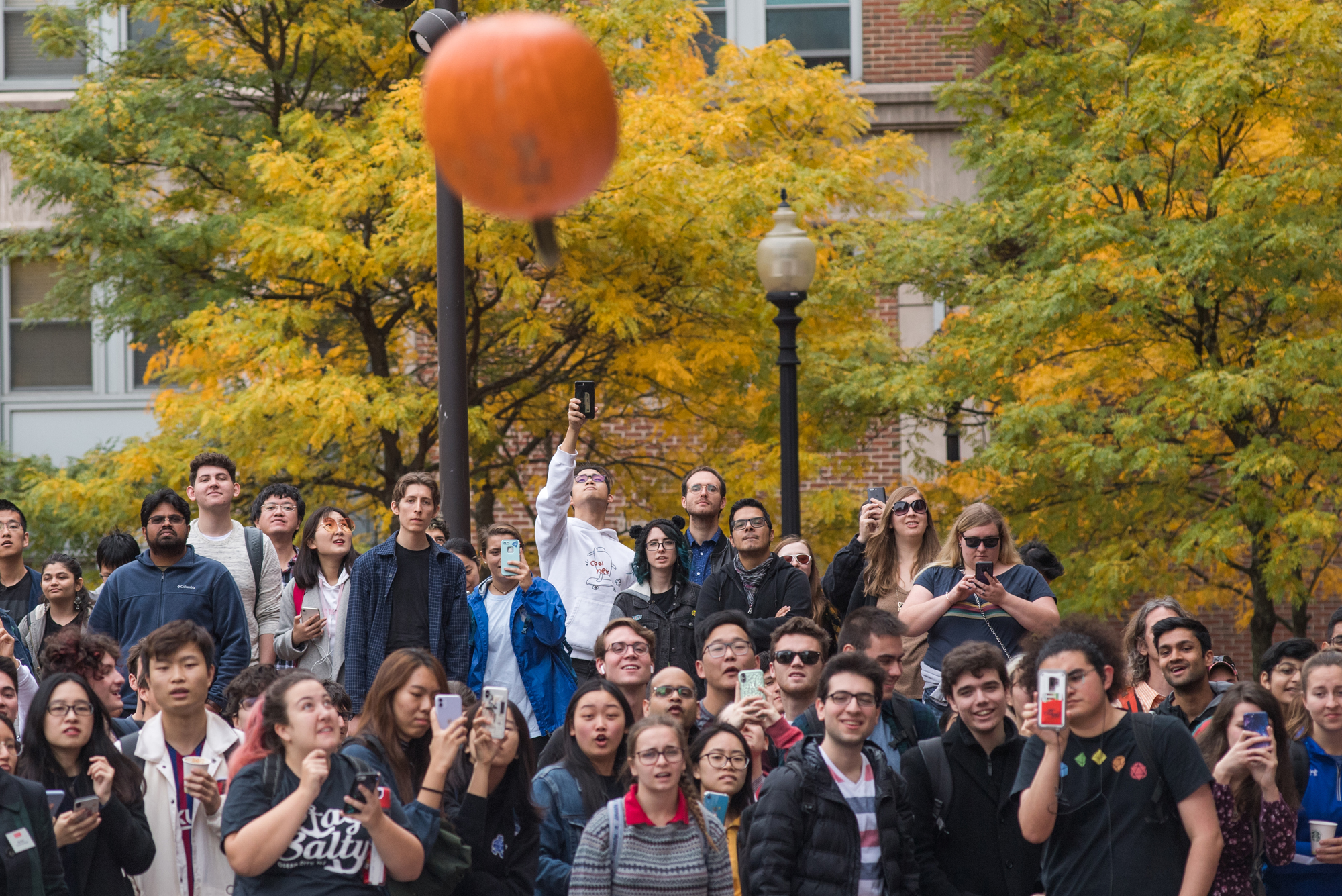 People gather and watch a pumpkin plummeting to the ground